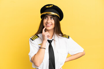 Airplane pilot isolated on yellow background thinking an idea while looking up