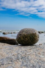 Large, rough-textured rock resting on a sandy beach near the edge of a blue ocean