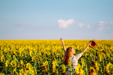 Fototapeta premium Beautiful woman strolling through field with sunflowers. Fashion, lifestyle, travel and vacations concept.