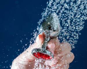 Woman washing silver butt plug under shower on blue background. 