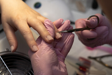 Obraz na płótnie Canvas Classical manicure. Hygiene and care for hands, beauty industry concept. Woman manicurist master is cutting cuticle using scissors on client's finger in beauty salon, closeup hands view.