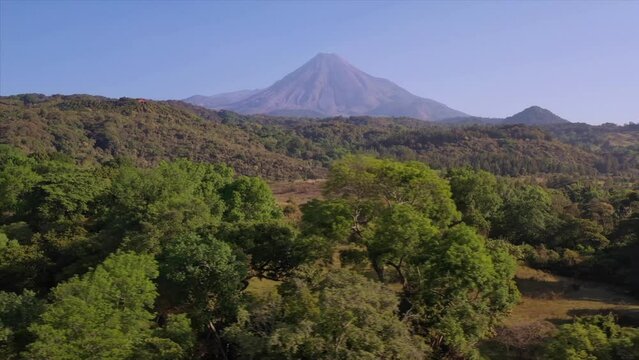 Vuelo de drone hacia la derecha sobre el bosque y teniendo en el horizonte el Volc&aacute;n de Fuego de Colima. M&eacute;xico.