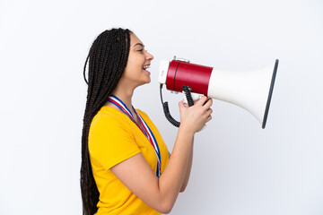 Naklejka premium Teenager girl with braids and medals over isolated pink background shouting through a megaphone