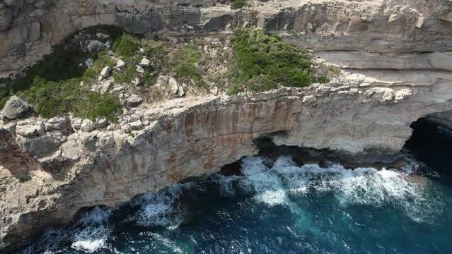 Aerial video of the sea waves crashing on the rocky shore covered with green grass
