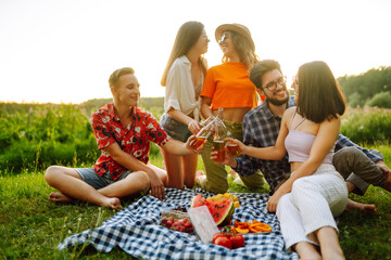 Group of young people  having fun while drinking beer,  talking at picnic party outside city on warm summer day. Vacation, picnic, friendship or holliday concept.