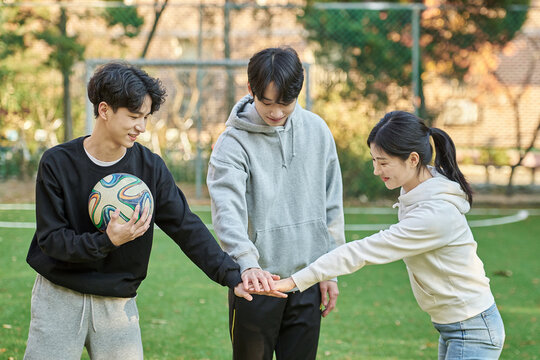 Three young male and female college models walk with a ball and raise their hands in celebration after a game at a fall college futsal field in South Korea, Asia. 