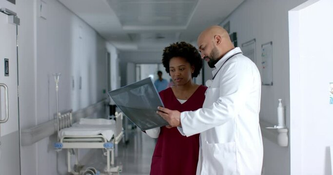 Diverse doctors discussing work and looking at x-ray scans in corridor, slow motion