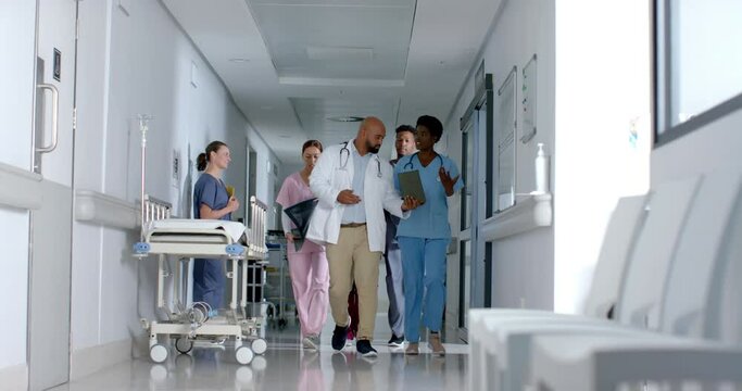 Diverse doctors using tablet and walking in corridor at hospital, slow motion