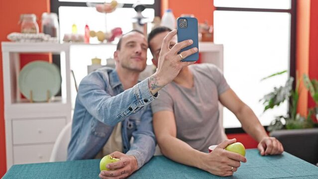 Two men couple make selfie by smartphone holding apple at dinning room