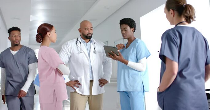 Diverse doctors discussing work and using tablet in corridor at hospital, slow motion