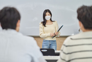 An Asian female student or professor is wearing a mask and standing in front of a lecture hall at a...