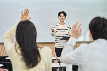 An Asian young man is standing in front of a lecture hall at a university in South Korea, giving a...