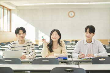 Three young Asian college students, both male and female, are in a classroom in South Korea where they are either teaching or studying