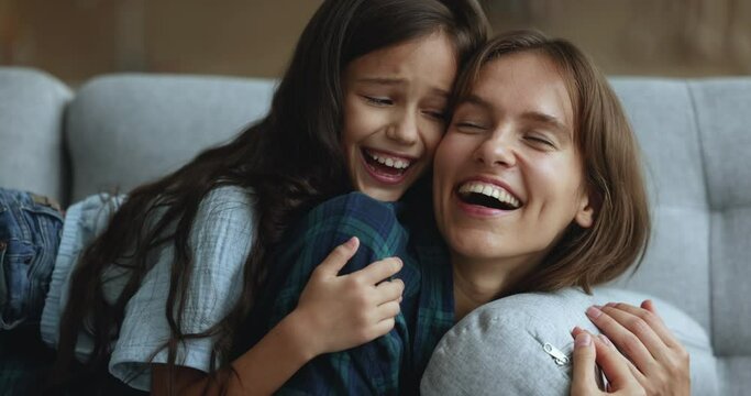 Closeup beautiful mother laughing, enjoy sweet moments lying on sofa with loving adorable daughter, spending leisure weekend time together at home. Happy Motherhood, family pastime, unconditional love