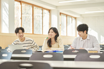 Three young Asian college students, both male and female, are in a classroom in South Korea where they are either teaching or studying