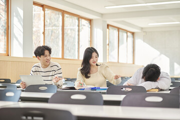 Three young Asian college students, both male and female, are in a classroom in South Korea where they are either teaching or studying