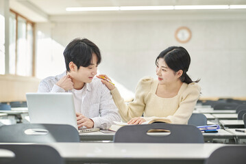 Fototapeta premium In a higher education classroom in South Korea, young university students are listening to a lecture, studying, and talking. A woman and a man are in the background