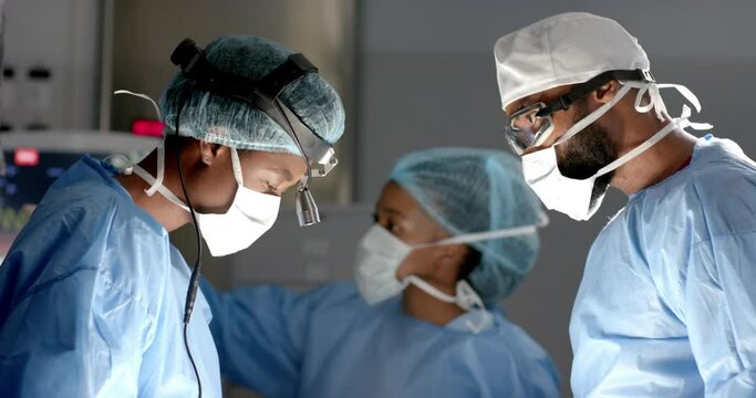 Diverse surgeons wearing surgical gowns operating on patient in operating theatre, slow motion
