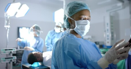 Portrait of african american female surgeon using tablet in operating theatre, slow motion - Powered by Adobe