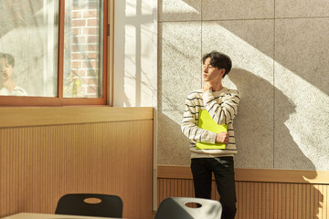 Young male college student models leaning against the wall of a university lecture hall in a...