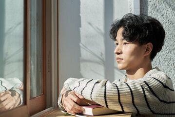 Young male college student models leaning against the wall of a university lecture hall in a light-filled room in South Korea, Asia