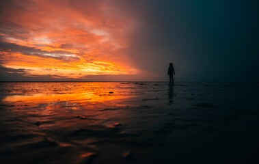 Fototapeta premium Silhouette of a person standing in shallow water against the sea at orange sunset