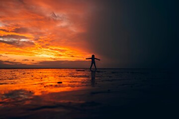 Silhouette of a person standing in shallow water against the sea at orange sunset