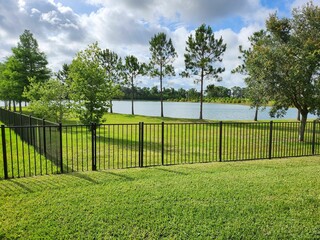 Sunny day in a park features a tranquil pond with a black fence and green trees.