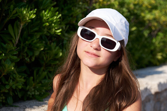 Portrait of beautiful girl with freckles in white cap and sunglasses on beach.
