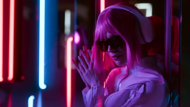 Beautiful woman with purple hair in futuristic costume over dark background. Violet neon light. Portrait of young girl in modern headphones listening music.