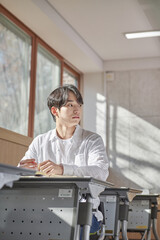 Fototapeta premium A young college student is sitting at a desk in a university classroom in South Korea, Asia. He is either reading a book or looking out of the window