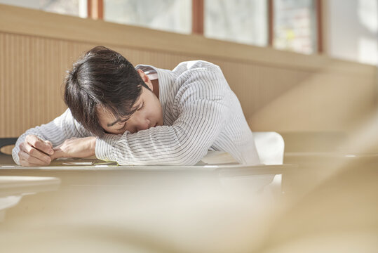 A Young Male College Student Is Sleeping On His Stomach On A Desk Inside A University Classroom In South Korea, Which Is In Asia