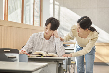 Girlfriend comforting a distressed young college male model sitting at a desk in a university...