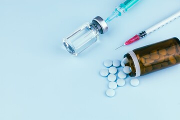 Syringe with a needle and various pills on a blue background