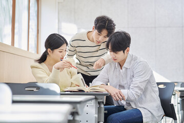 Three young male and female college students models sitting or standing at desks in a university...