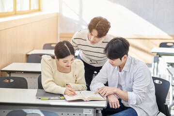 Obraz premium Three young male and female college students models sitting or standing at desks in a university classroom in South Korea, Asia, talking or having a discussion