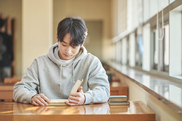 Asian Korean University Library Young male college student model sitting at a desk by a window with...