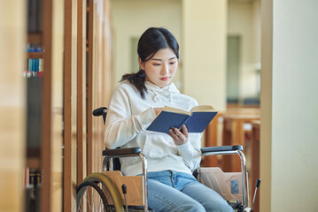 A young female college student with a disability is reading a book in a wheelchair at a university...