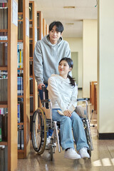 Young handicapped female college student model with disability sitting in wheelchair and reading...