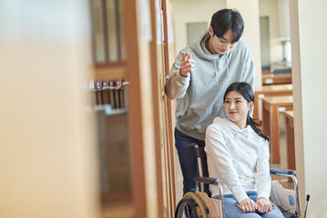 Young handicapped female college student model with disability sitting in wheelchair and reading...