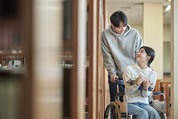 Young handicapped female college student model with disability sitting in wheelchair and reading...