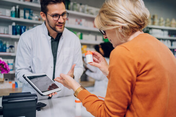 Portrait of a male pharmacist helping a senior woman patient in pharmacy