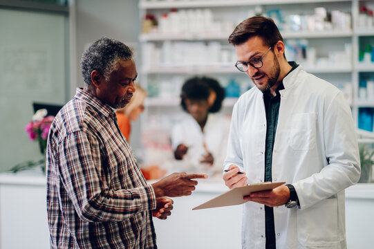 Male pharmacist helping a senior african american man patient in pharmacy