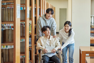 A young male model with a disability sitting in a wheelchair reading a book in a university library...