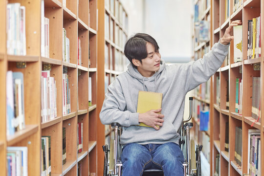 Asia South Korea university library bookcase in a wheelchair looking for a book on the shelf, physically handicapped young disabled male college student model