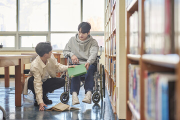 Young handicapped disabled male college student model in wheelchair looking for books in library...