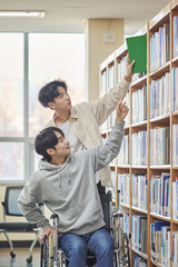 Young handicapped disabled male college student model in wheelchair looking for books in library...