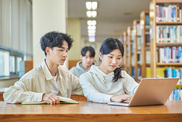 Two young college student man and woman couple model and solo male model looking at laptop and book together in library of Asian Korean university