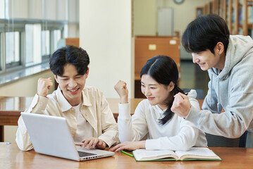 Two young college student man and woman couple model and solo male model looking at laptop and book together in library of Asian Korean university