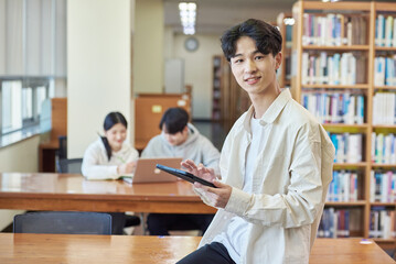 Young Asian Korean male model, man and woman model and looking out the window with tablet in the library on the background of bookshelf